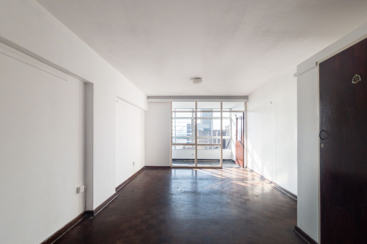 A spacious, empty living area featuring original parquet flooring and a large glass partition, offering a bright and open layout ready for renovation.