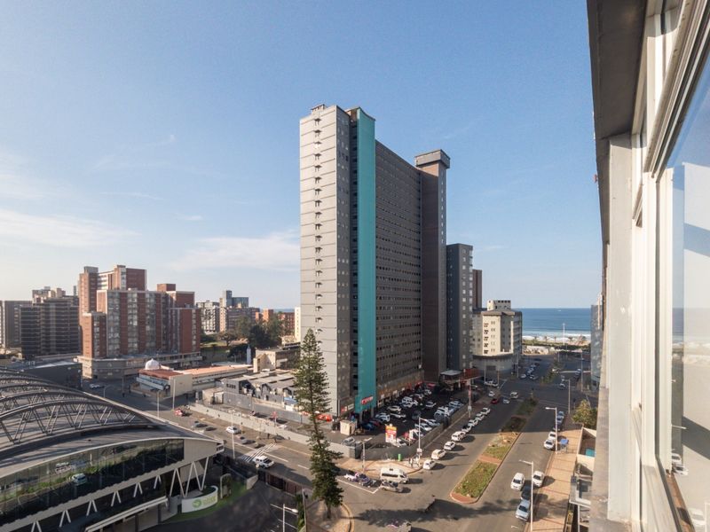 Elevated urban view overlooking a high-rise apartment complex, surrounding city streets, and distant coastline.