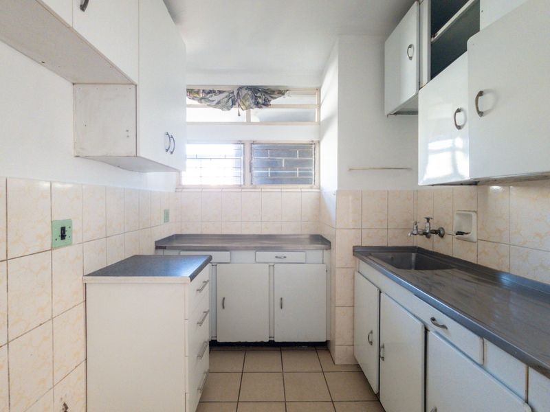 A functional, dated kitchen featuring built-in cabinetry, stainless steel countertops, a sink, and tiled finishes, offering a blank canvas for modern renovation.