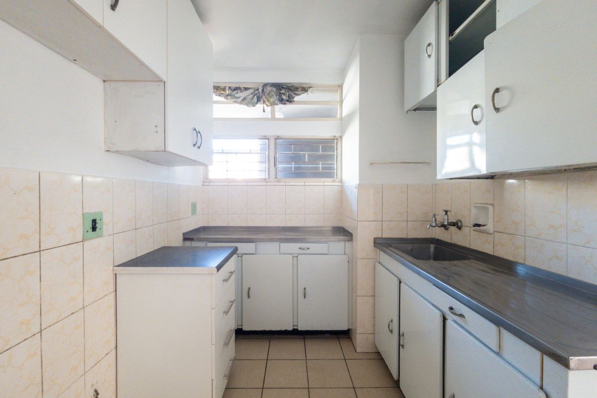 A functional, dated kitchen featuring built-in cabinetry, stainless steel countertops, a sink, and tiled finishes, offering a blank canvas for modern renovation.