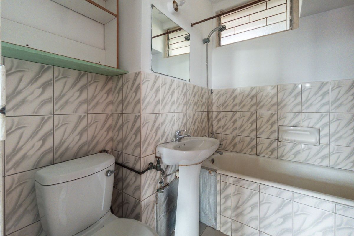 A dated bathroom featuring a pedestal sink, bathtub with shower head, and tiled walls. The space is empty and ready for renovation.