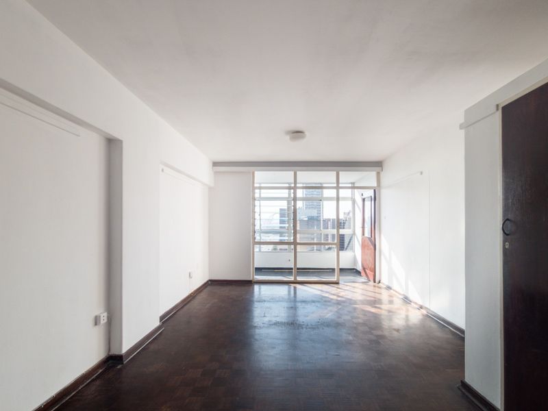 A spacious, empty living area featuring original parquet flooring and a large glass partition, offering a bright and open layout ready for renovation.