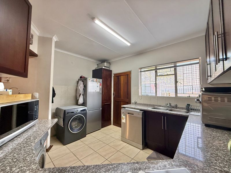 Functional kitchen featuring granite countertops, double basin sink, and ample built-in cabinetry with tiled flooring and a window with security bars.
