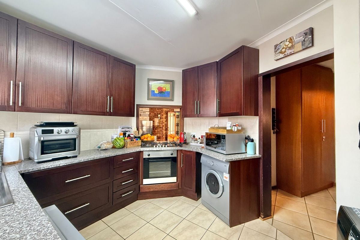 A functional kitchen featuring dark wood cabinetry, granite countertops, built-in oven, gas hob, and tiled flooring, offering a practical layout for daily meal preparation.
