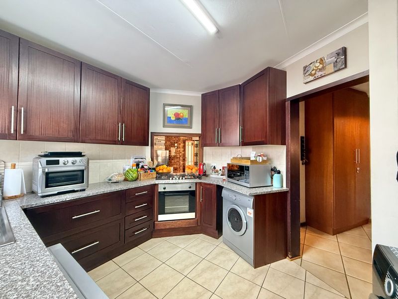 A functional kitchen featuring dark wood cabinetry, granite countertops, built-in oven, gas hob, and tiled flooring, offering a practical layout for daily meal preparation.