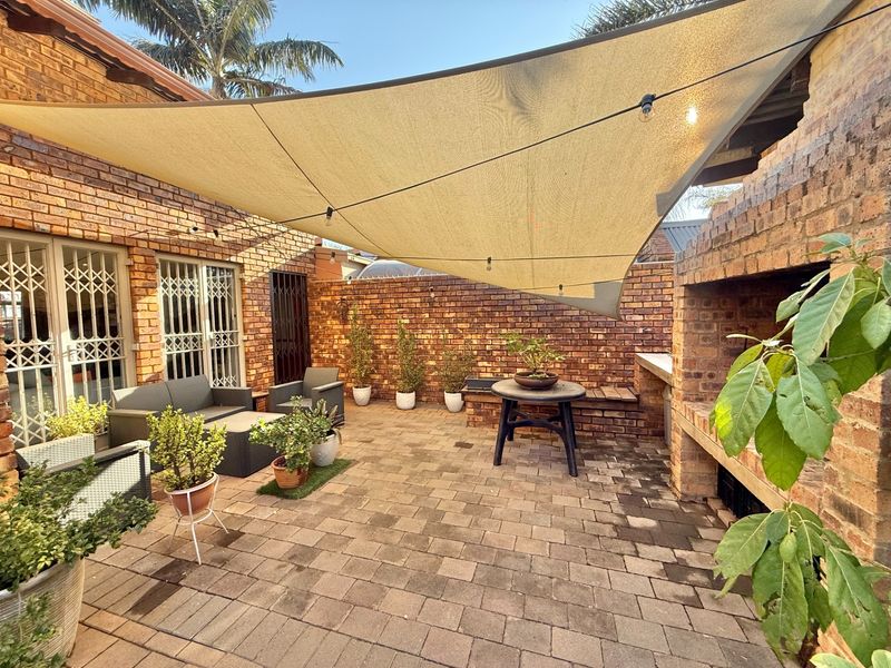 A private outdoor patio area featuring a built-in brick braai, paved flooring, and a shade sail, perfect for outdoor entertaining.