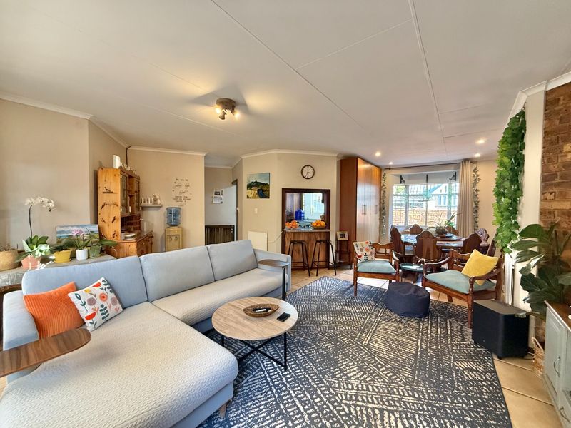 Spacious open-plan living and dining area featuring tiled floors, an exposed brick accent wall, and a convenient pass-through window to the kitchen.