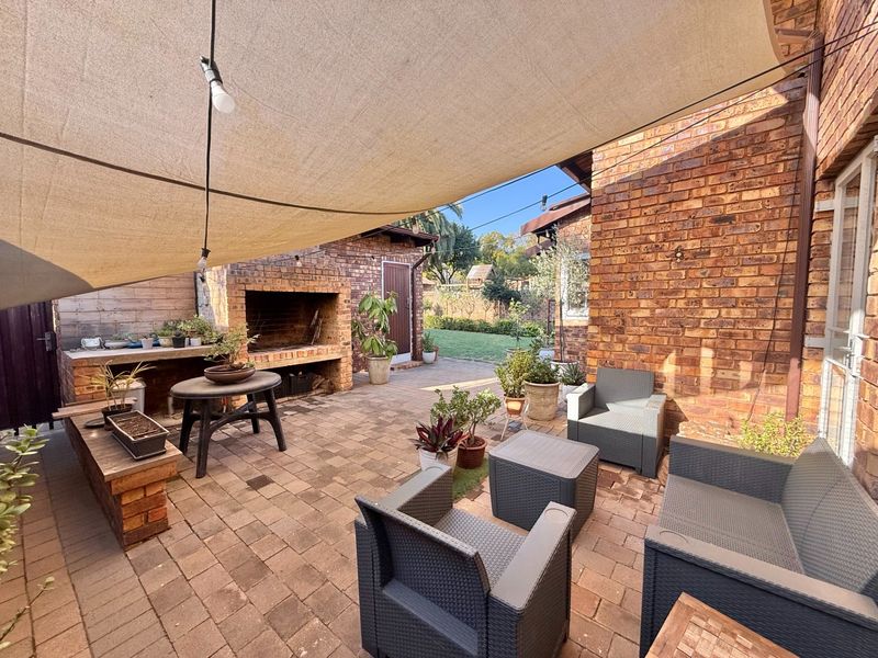 A covered outdoor patio area featuring exposed brick walls, a built-in braai, and brick paving, ideal for entertaining.