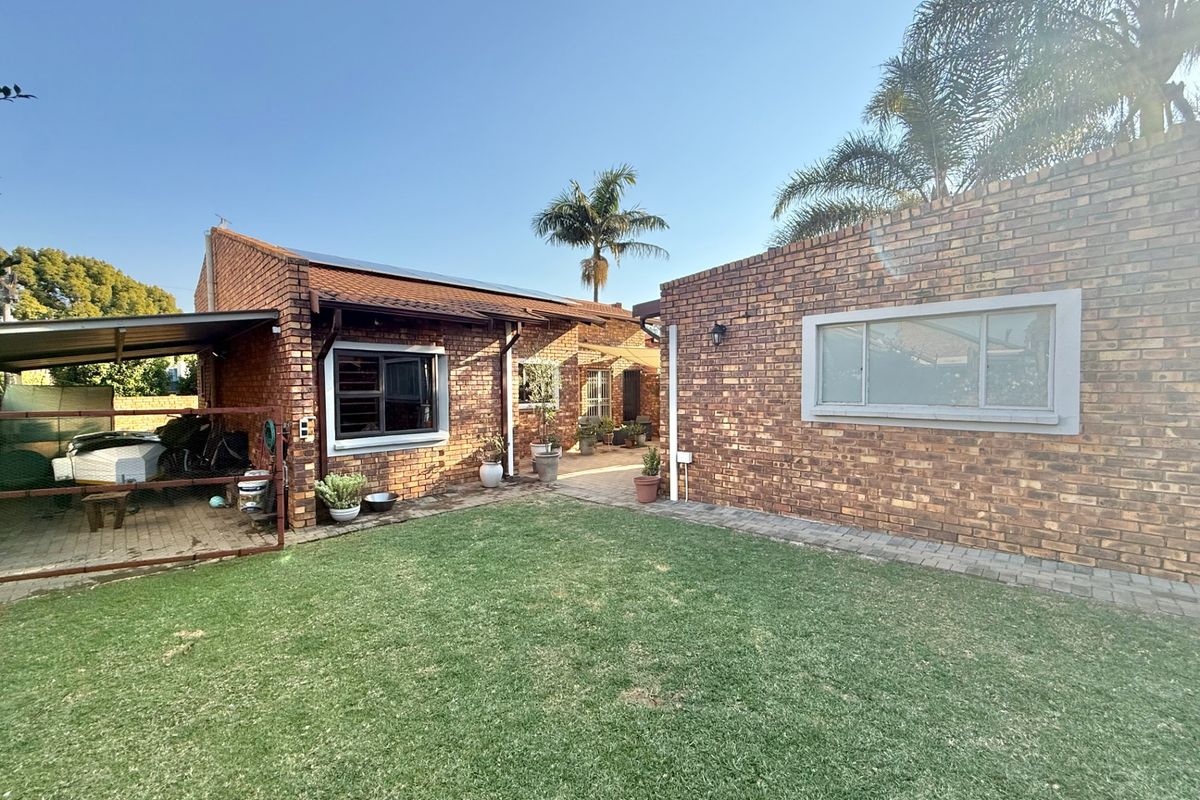 Rear view of the property featuring a face brick facade, a well-maintained lawn, paved patio area, and a covered carport structure.