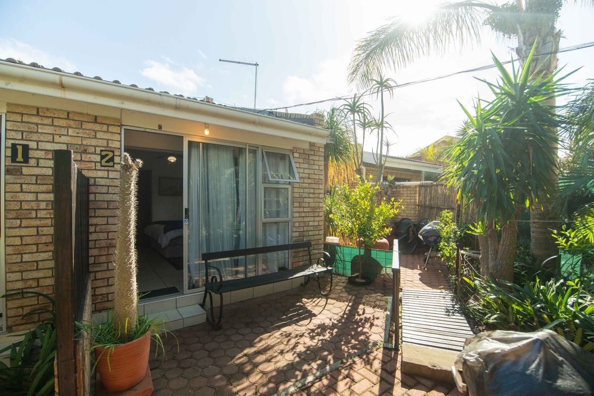 A rear exterior view of the property featuring a brick facade, sliding glass door access, and a paved patio area.