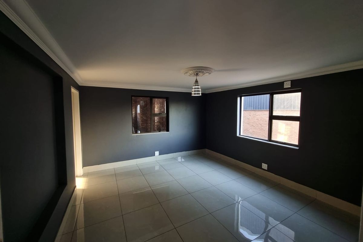 A spacious, empty living area featuring dark painted walls, polished tiled flooring, and modern ceiling detailing with a central pendant light.