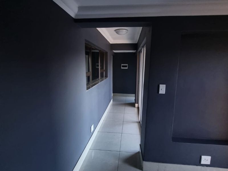 A clean, modern hallway featuring dark painted walls, neutral tiled flooring, and a recessed wall niche, leading towards a sliding glass door.