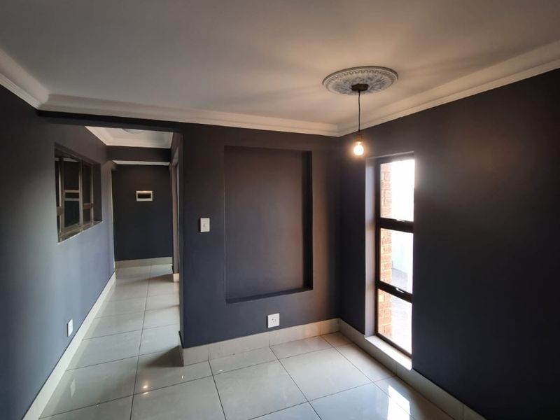 A clean, modern hallway featuring dark painted walls, polished floor tiles, a decorative ceiling rose, and a recessed wall niche.