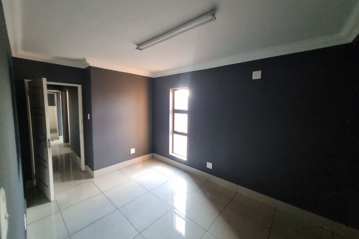 A clean, empty bedroom featuring dark painted walls, white tiled flooring, and a single window providing natural light.