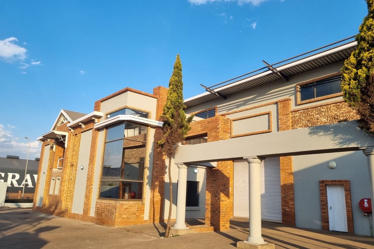Front elevation of a modern industrial building featuring a combination of brick and rendered finishes, large glass windows, and a roller shutter door.