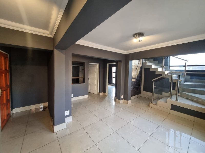Spacious open-plan interior featuring modern tiled flooring, a contemporary staircase with stainless steel balustrades, and neutral grey wall finishes.