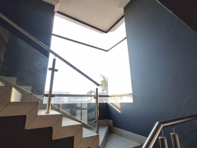 A modern staircase featuring tiled steps, a glass balustrade with stainless steel handrails, and a large window providing ample natural light.