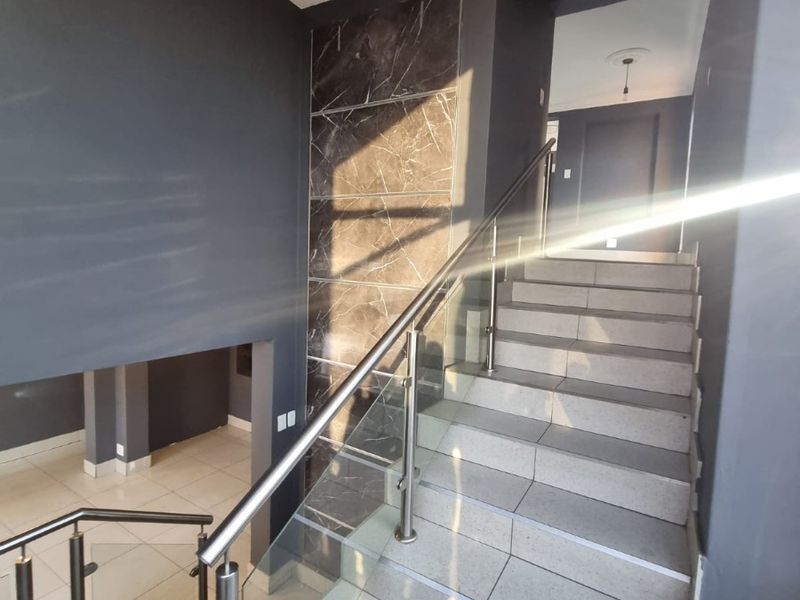 Modern industrial-style hallway featuring a tiled staircase with a glass and stainless steel balustrade and elegant marble-look wall accents.