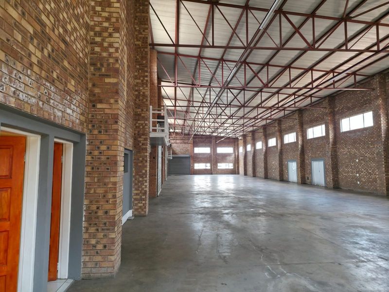 Spacious industrial warehouse unit featuring exposed brick walls, high steel roof trusses, concrete flooring, and multiple windows for natural light.