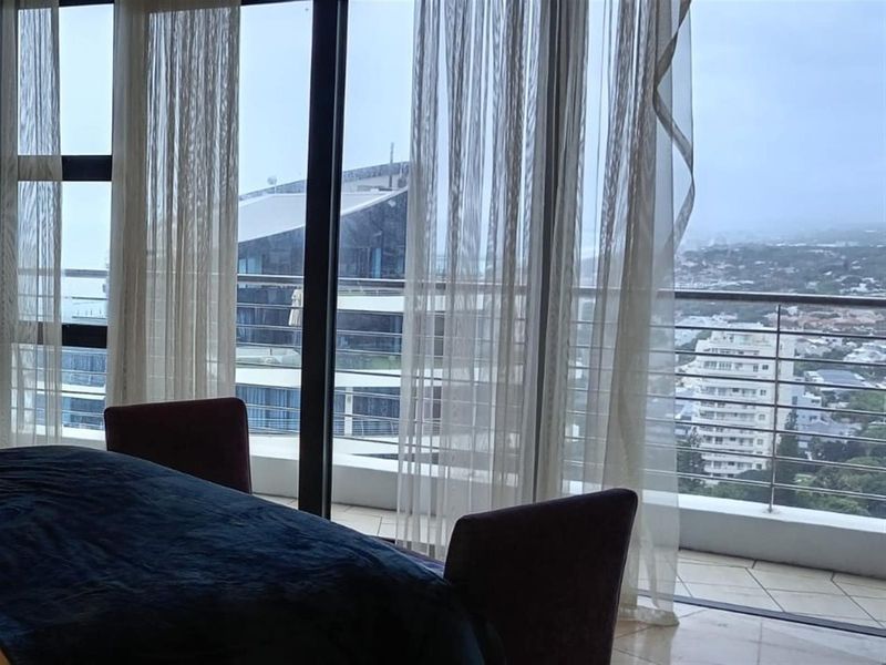 A view from an interior space looking out through large sliding glass doors onto a balcony with a metal railing and urban cityscape.