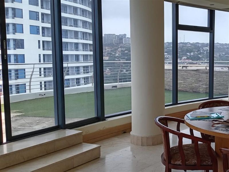 Spacious living area featuring floor-to-ceiling windows, marble flooring, and a raised platform, offering views of the adjacent terrace and surrounding urban landscape.
