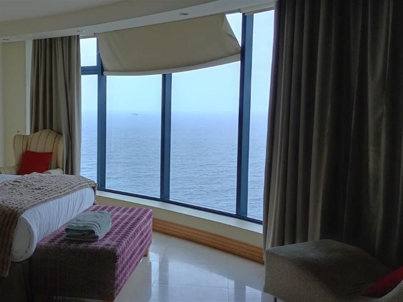 Spacious bedroom featuring expansive floor-to-ceiling windows with direct ocean views and integrated ceiling lighting.