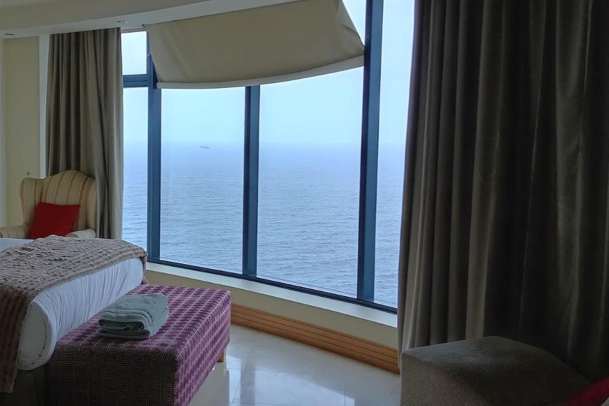 Spacious bedroom featuring expansive floor-to-ceiling windows with direct ocean views and integrated ceiling lighting.