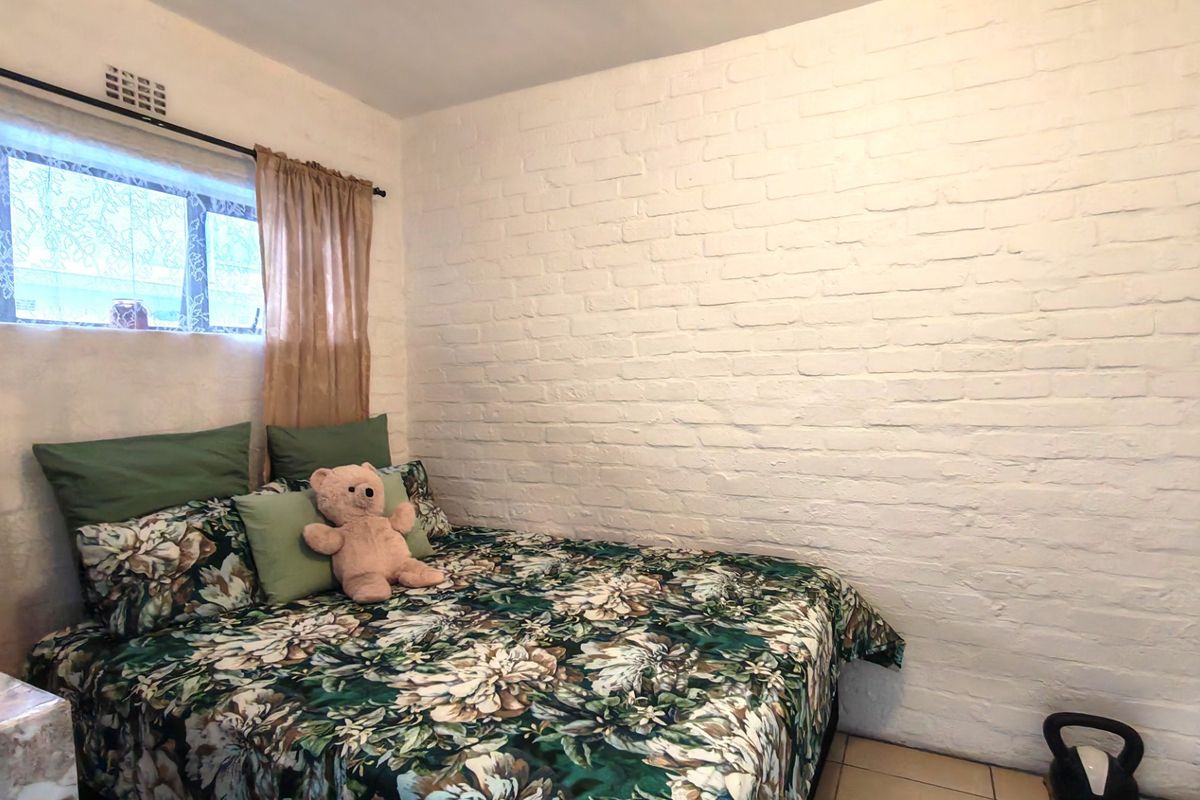 A bedroom featuring a white painted brick feature wall, tiled flooring, and a built-in cupboard, offering a neutral foundation for interior design.