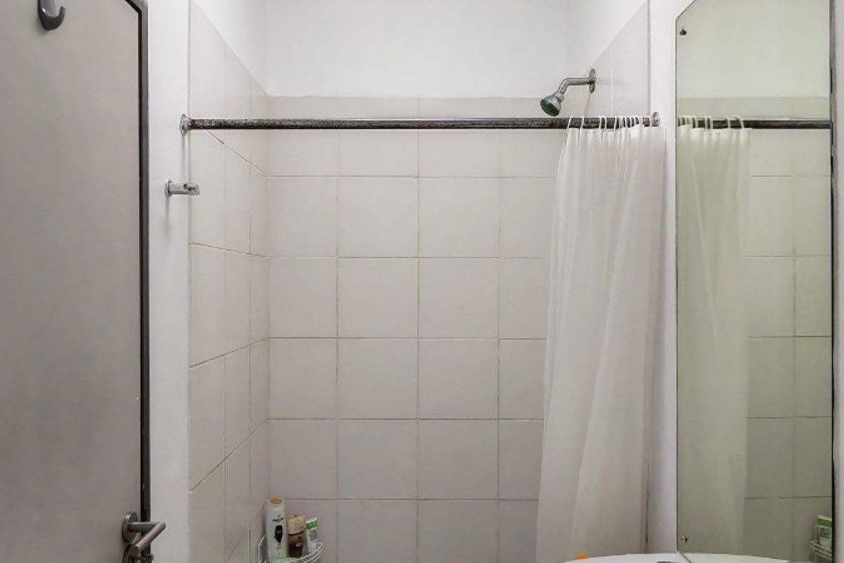 A functional bathroom featuring a wall-mounted basin, a tiled shower enclosure with a shower head, and a large wall mirror.