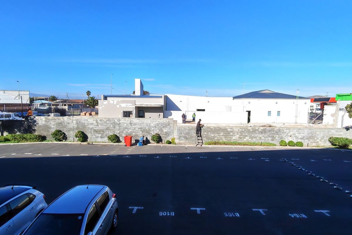 Rear view of the property showing an asphalt parking area and a boundary wall with ongoing exterior maintenance and plastering work.