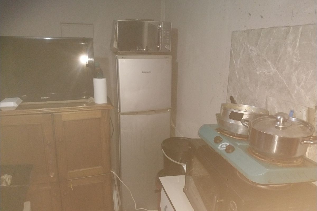 A small, basic kitchen area featuring a marble-effect splashback, currently utilized with freestanding appliances and limited fixed infrastructure.