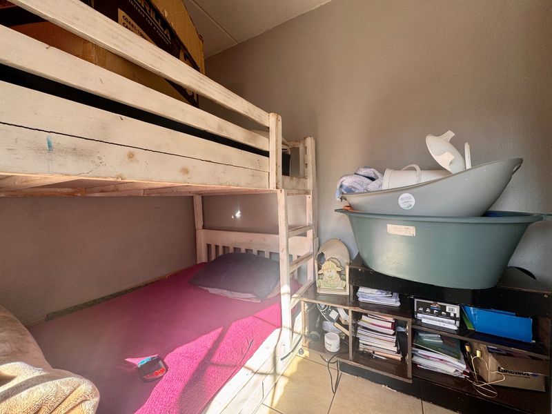 A compact bedroom featuring tiled flooring, currently utilized for storage and sleeping arrangements.