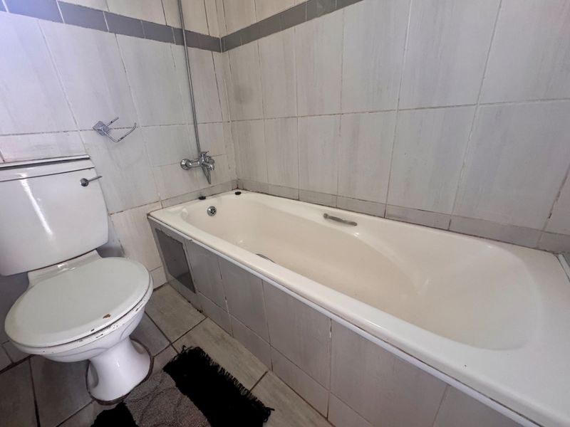 A functional bathroom featuring a standard bathtub with shower mixer and a toilet, finished with ceramic wall and floor tiling.