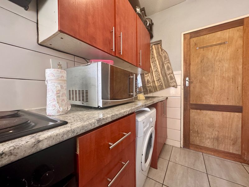 Compact kitchen featuring wooden cabinetry, laminate countertops, tiled backsplash, and integrated appliances, providing a functional workspace with potential for cosmetic updates.