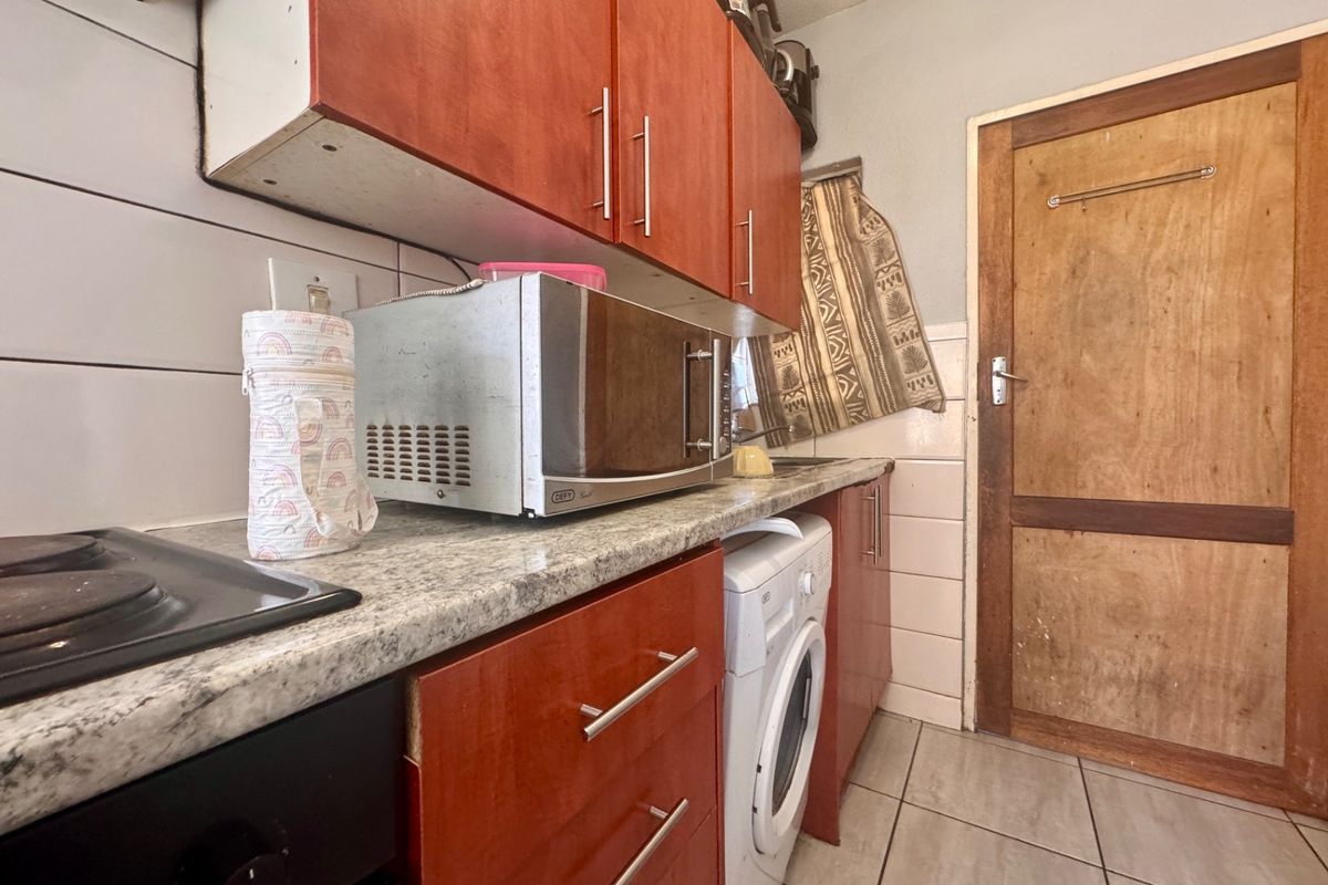 Compact kitchen featuring wooden cabinetry, laminate countertops, tiled backsplash, and integrated appliances, providing a functional workspace with potential for cosmetic updates.