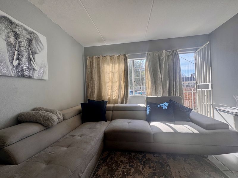 A living room featuring tiled flooring, a window, and a security gate leading to an outdoor area.