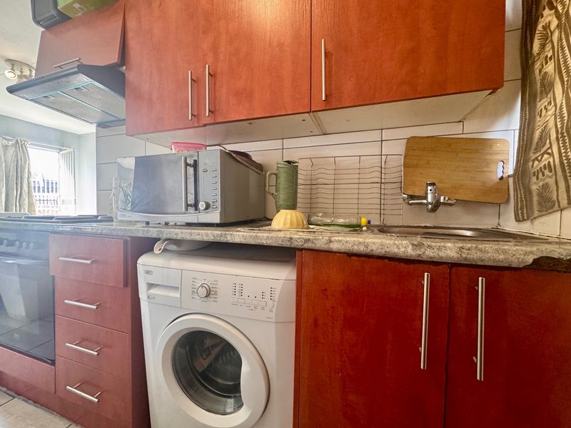 Compact kitchen featuring wood-look cabinetry, laminate countertops, built-in oven with extractor fan, and an integrated washing machine.