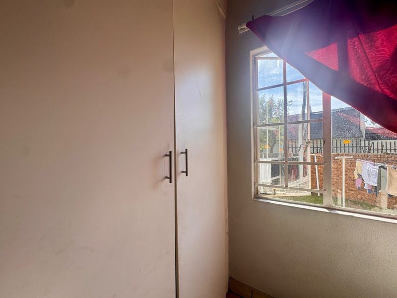 A bedroom featuring a built-in wardrobe and a window with security burglar bars, offering a view of the exterior area.