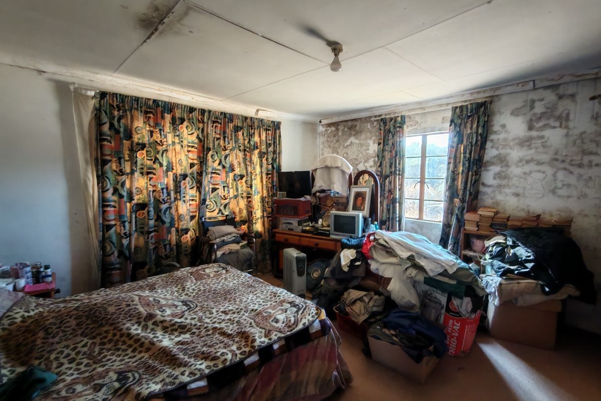 A bedroom requiring significant renovation, featuring visible wall plaster damage and ceiling staining, offering a blank canvas for complete refurbishment.