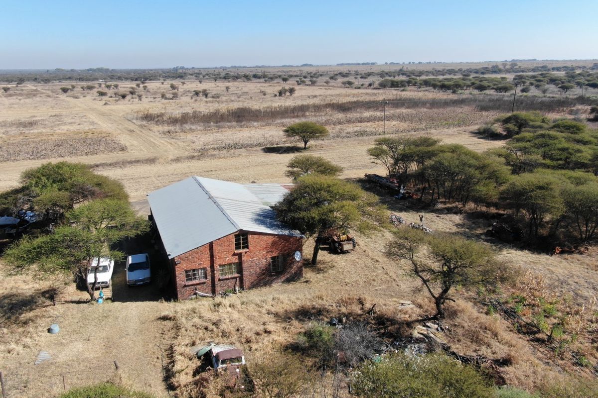 Aerial view of a rural farm property featuring an exposed brick building with a corrugated metal roof set within a large open landscape.