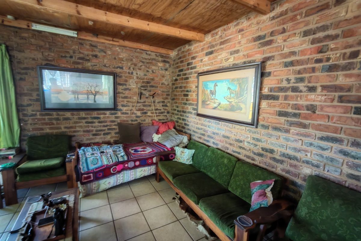 A rustic living room featuring exposed brick walls, a timber beam ceiling, and ceramic floor tiles, offering a warm and traditional farm-style aesthetic.