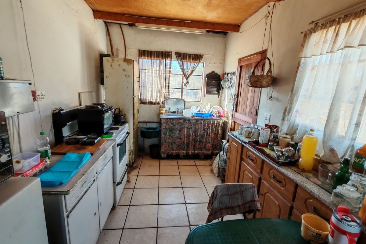 A dated kitchen featuring ceramic tile flooring, exposed timber ceiling beams, and original cabinetry, requiring significant renovation to modernize the space.