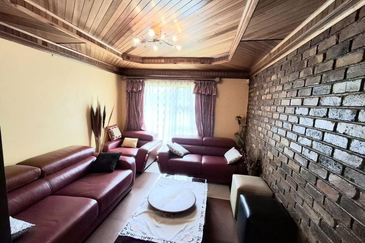 A living room featuring a distinctive timber tongue and groove ceiling and an exposed brick feature wall.