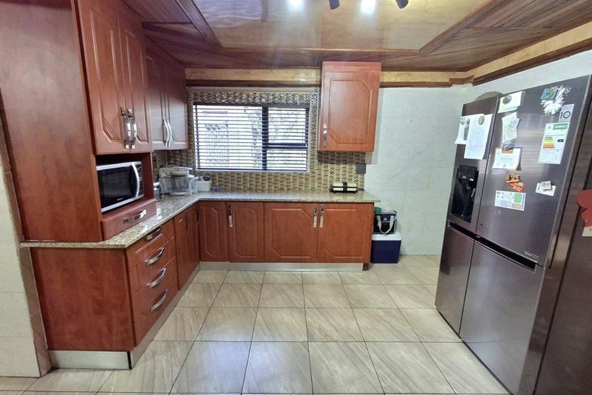 A functional kitchen featuring wood-finish cabinetry, granite countertops, tiled backsplash, and tiled flooring with integrated lighting.