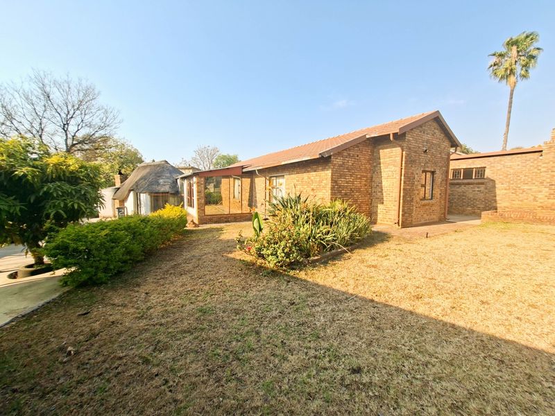 Rear view of a face brick house featuring a tiled roof, a small paved patio area, and an adjacent thatched roof structure in the garden.