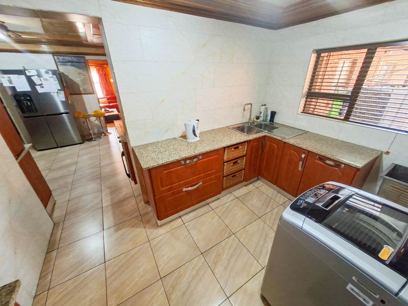 A functional kitchen featuring wooden cabinetry, granite countertops, tiled walls, and tiled flooring, with a view into the adjacent living area.
