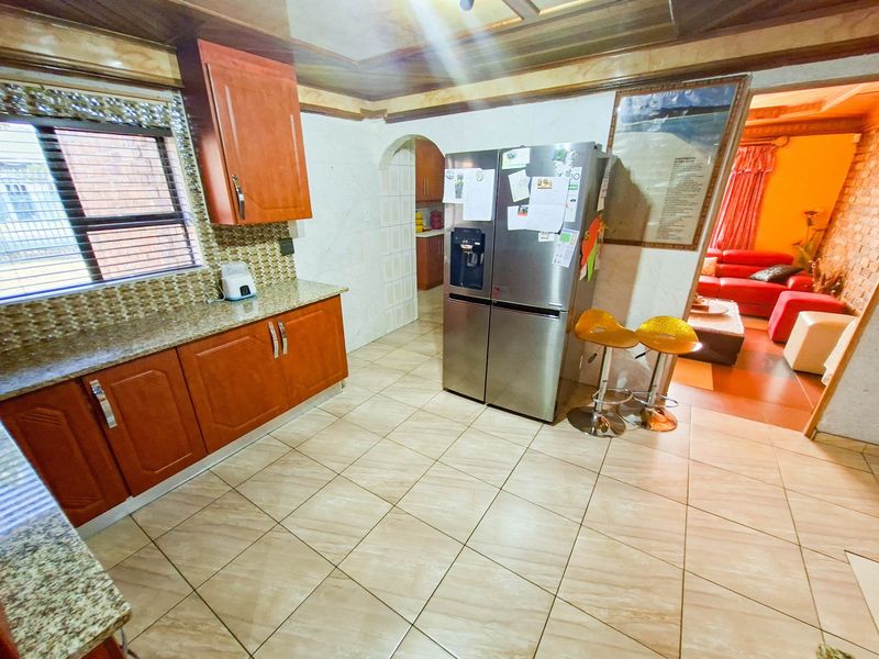 A functional kitchen featuring wooden cabinetry, granite countertops, and tiled flooring, with an open archway leading into the adjacent living area.