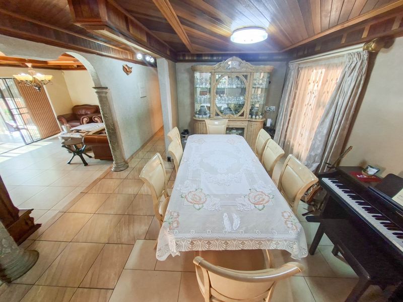 A formal dining room featuring a timber ceiling, tiled flooring, and an arched entryway leading to an adjacent living area.