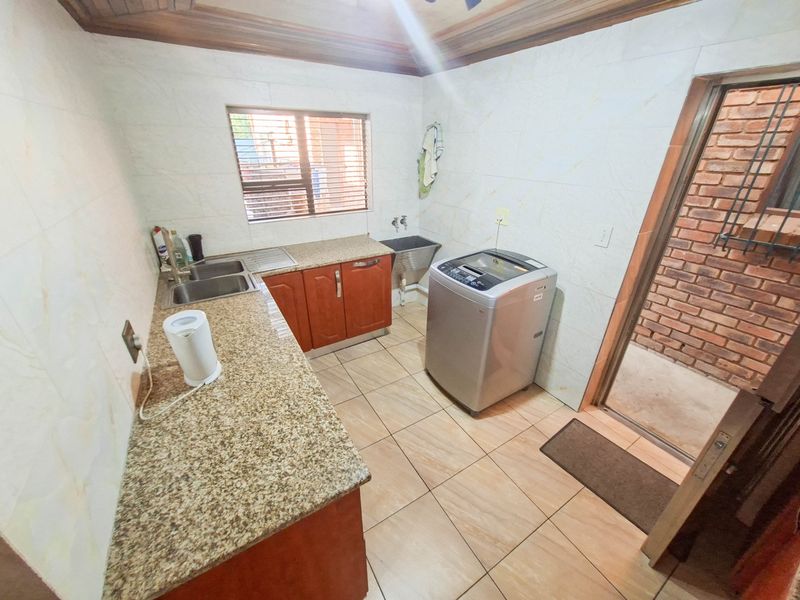 A functional laundry room featuring granite countertops, a stainless steel sink, tiled walls, and tiled flooring with direct access to an exterior area.