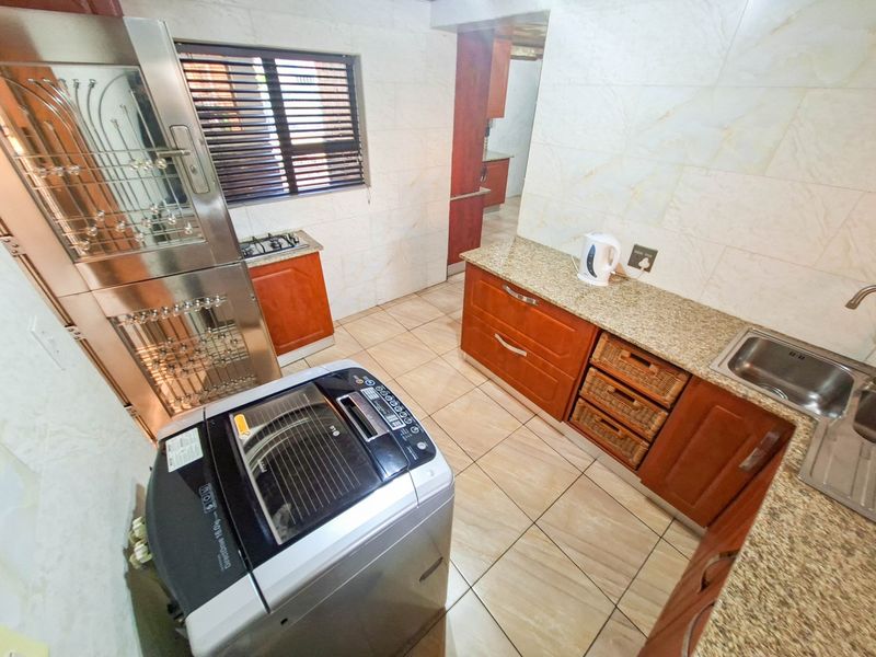 A functional kitchen featuring granite countertops, wooden cabinetry, tiled finishes, and a gas hob, with an adjacent scullery area visible.